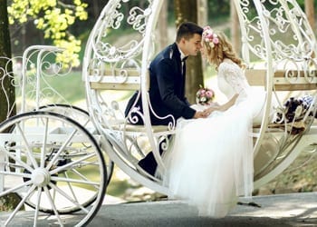 A couple sit inside a white horse-drawn carriage during their wedding