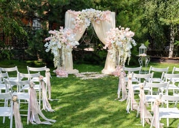 An outdoor wedding arch decorated with floral arrangements and luxurious drapes.